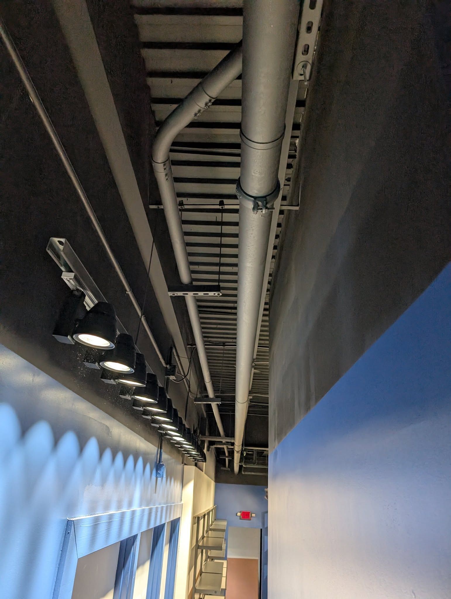 Narrow hallway with lights, pipes, and a blue wall.