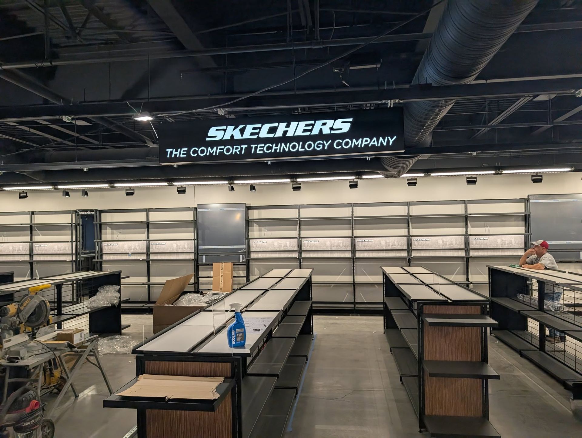 Empty Skechers store interior with shelving, workers, and the company sign.