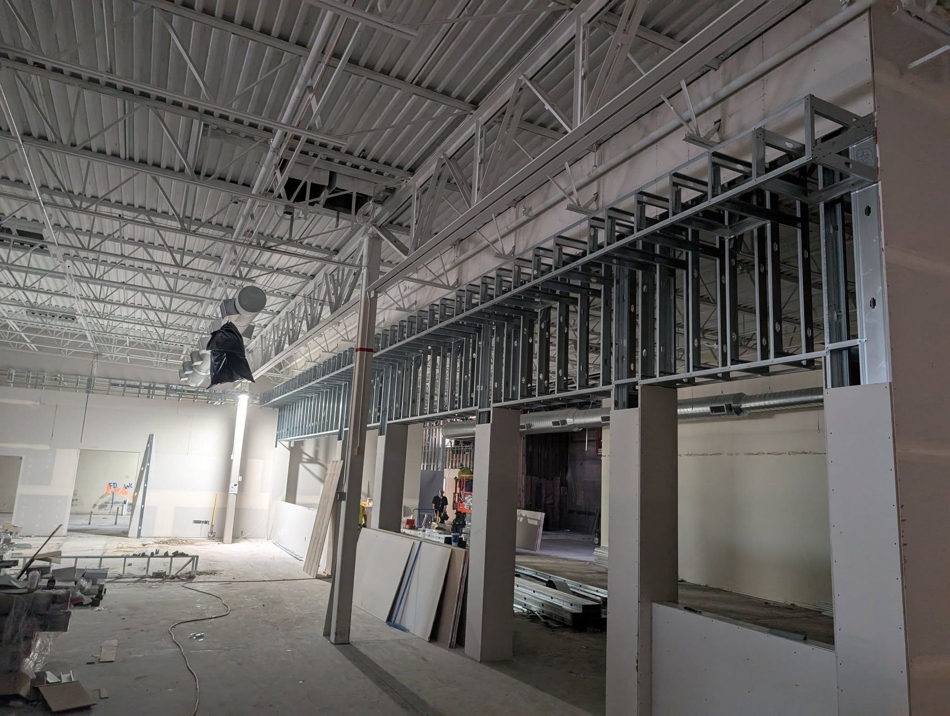 Construction site with exposed metal framing, drywall, and high ceilings.