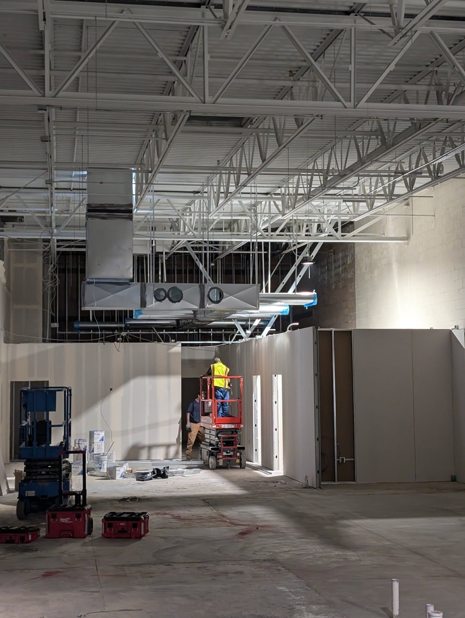 Construction site: Worker on lift; HVAC and metal beams visible. Interior view with unfinished walls.