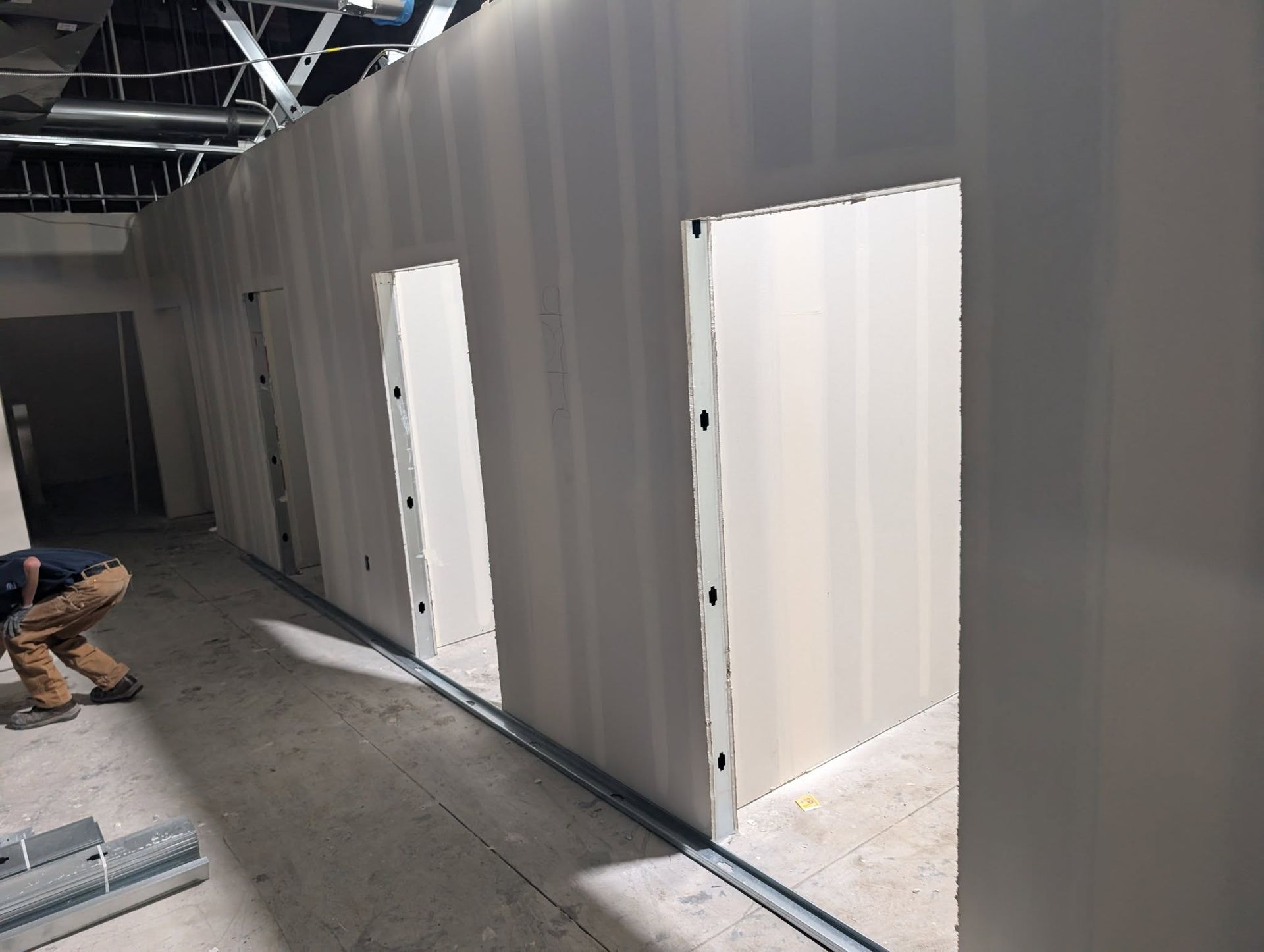Construction of interior drywall walls with door frames; worker visible.