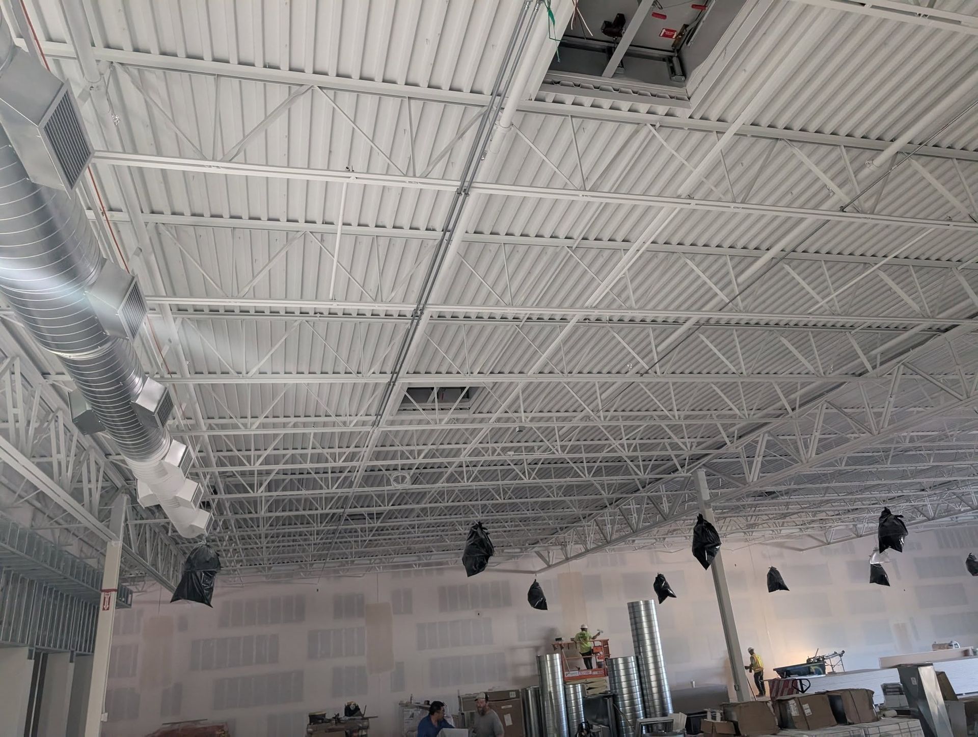 White metal ceiling in a building under construction, with exposed beams, ductwork, and ventilation shafts.