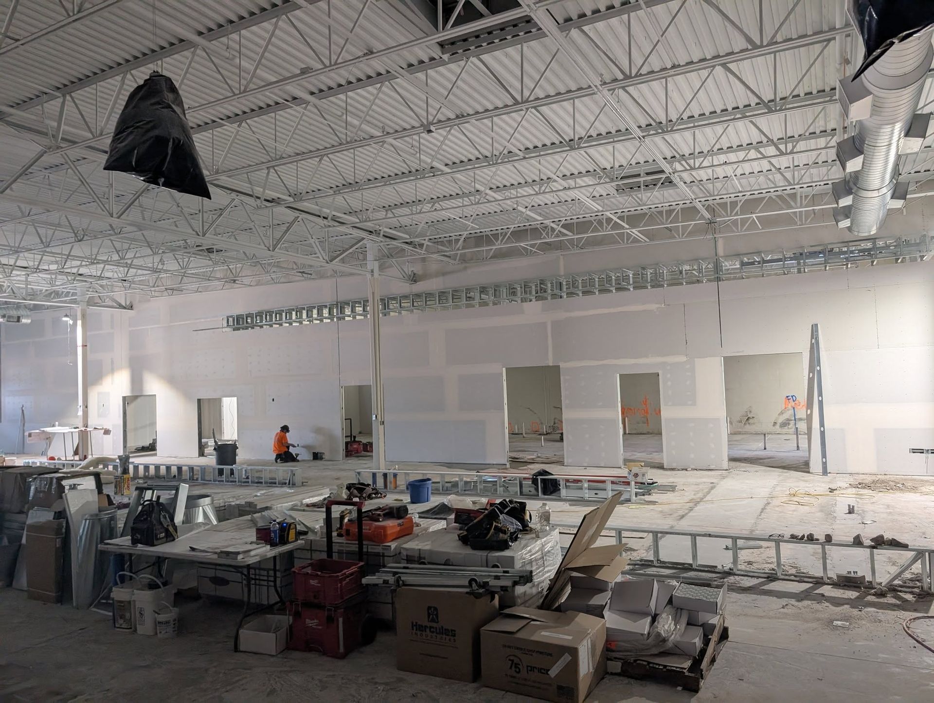 Construction in a large open space, walls being built, materials and tools scattered.