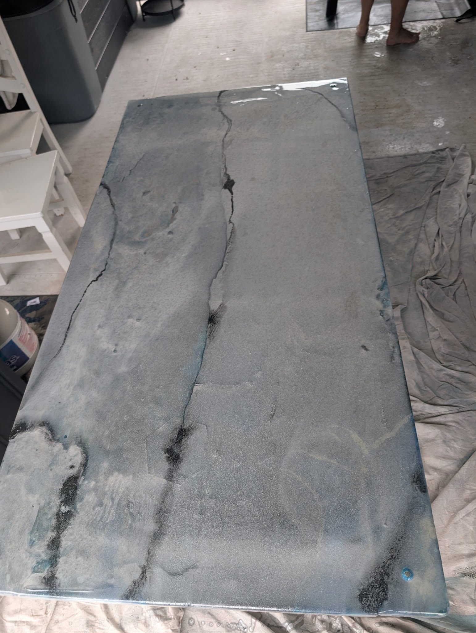 A rectangular, gray epoxy-coated countertop with black veins. White stool and bucket in the background.