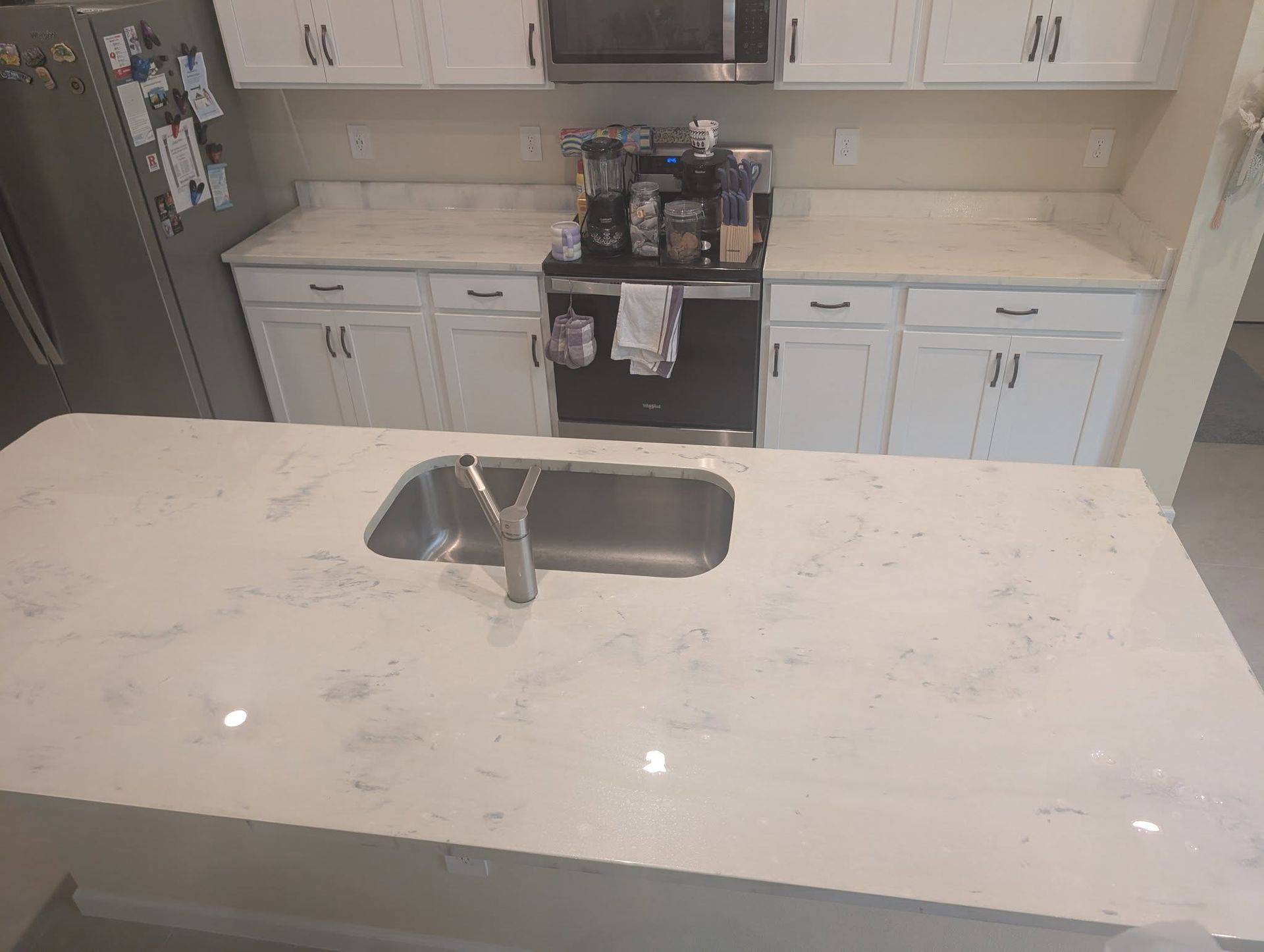 White kitchen with island and sink. Stainless steel appliances. White cabinets and countertops.