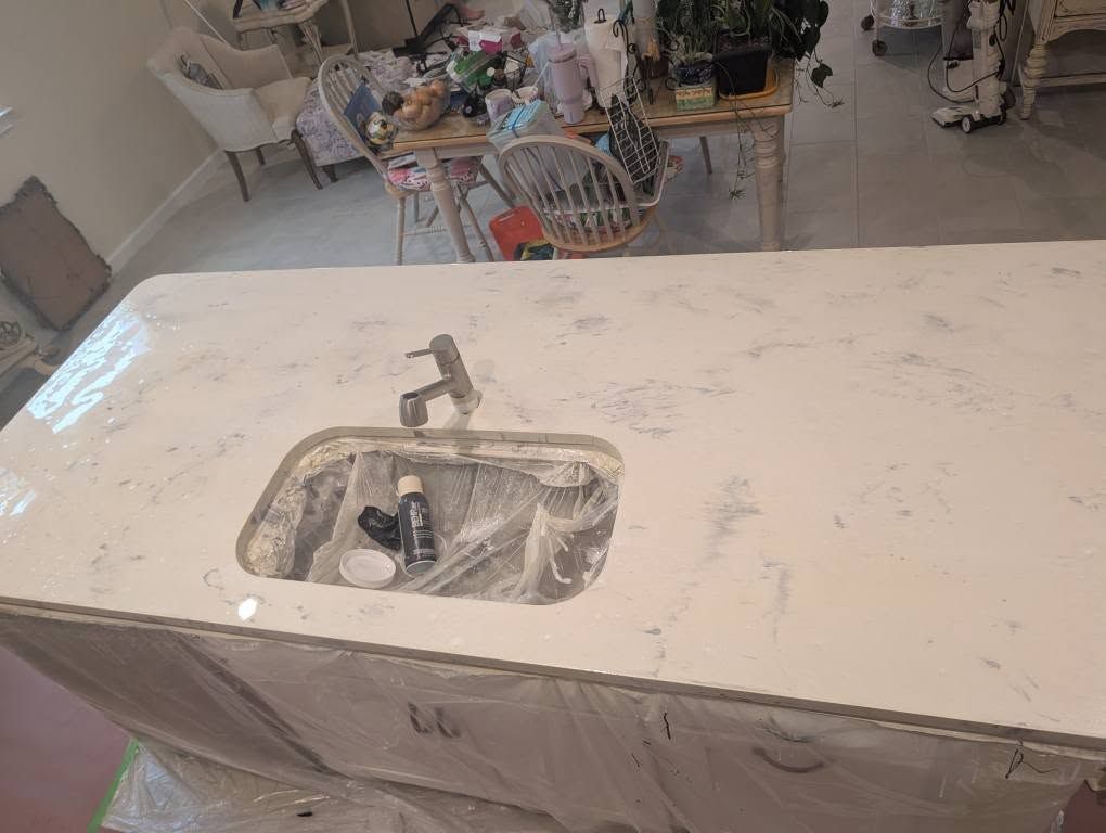 White countertop with a sink cut-out and faucet. The surface has a marble-like pattern; the kitchen in the background.