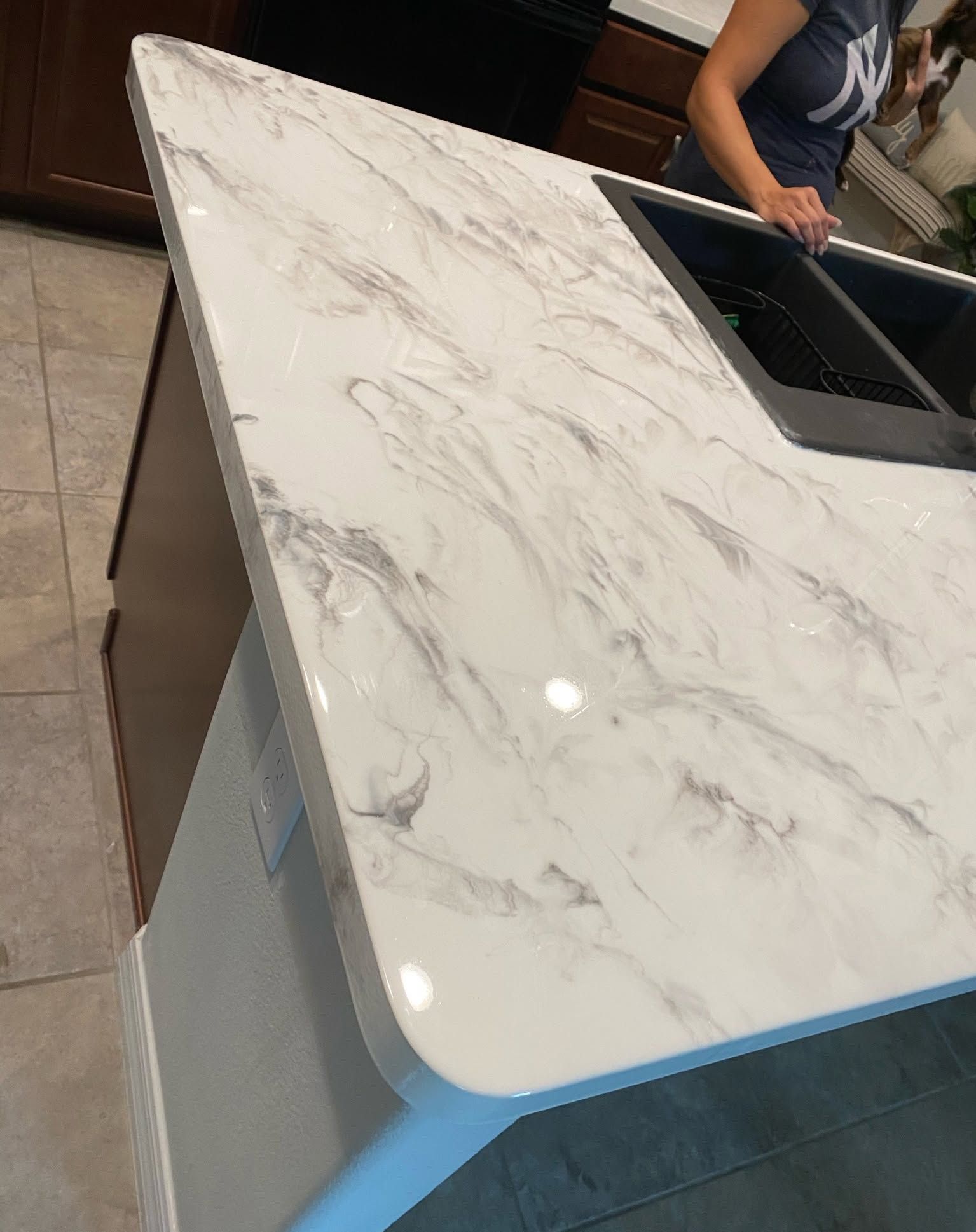 White marble countertop with grey veining, a black sink, and a person in a blue shirt.