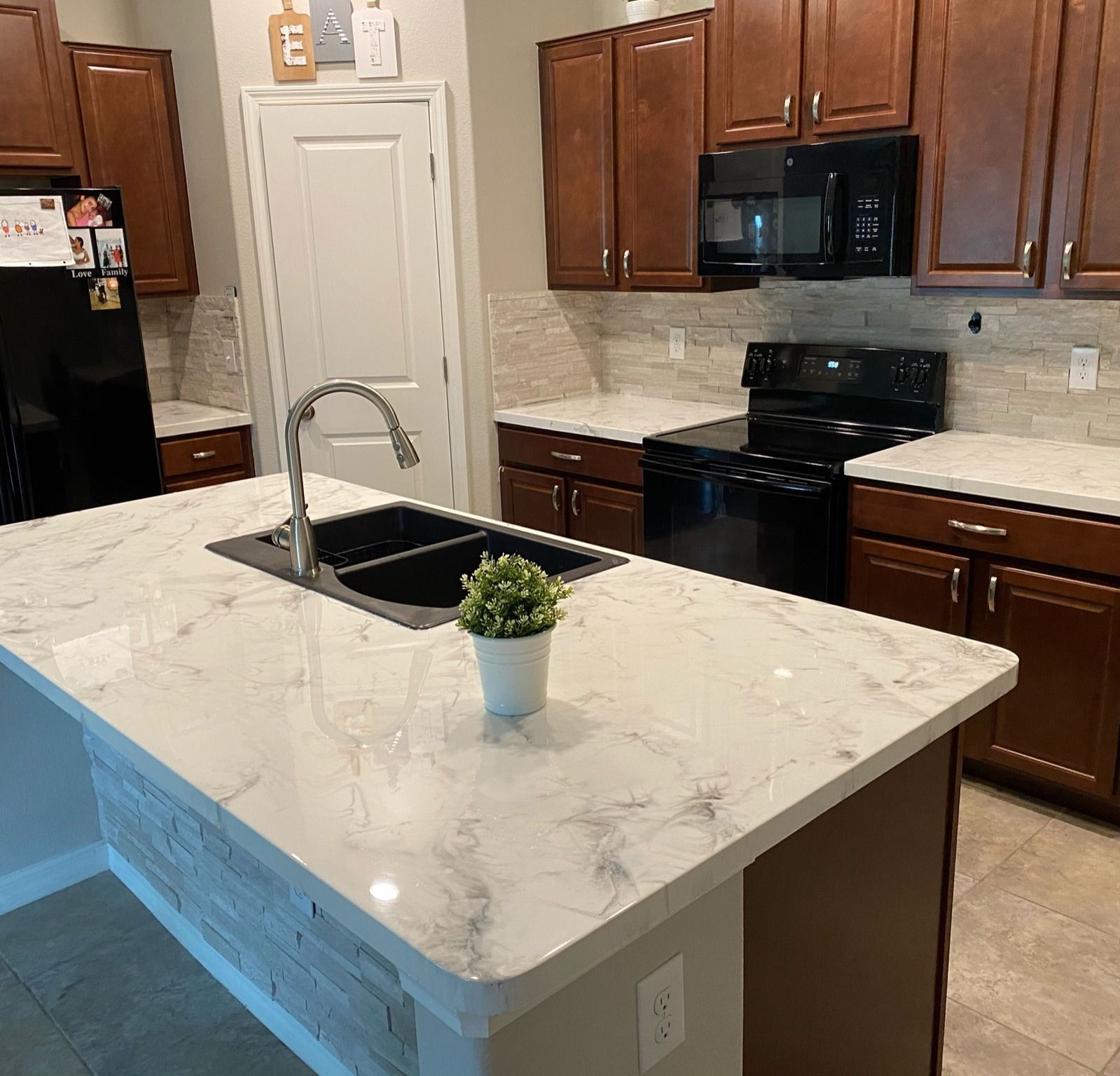 Kitchen with dark brown cabinets, black appliances, white countertops, and a stone-faced island.