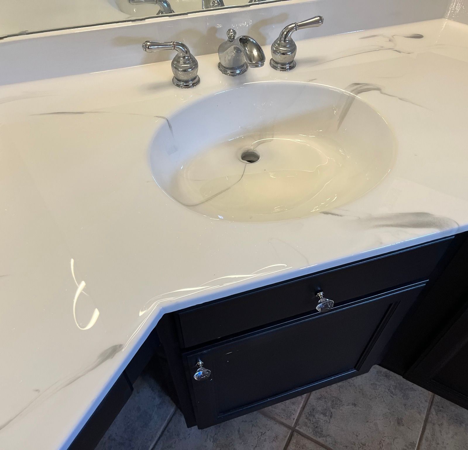 White marble countertop with oval sink, chrome fixtures, and dark brown cabinet.