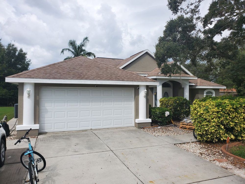 Tan house with white garage door and columns. Bicycle in the driveway. Cloudy sky.