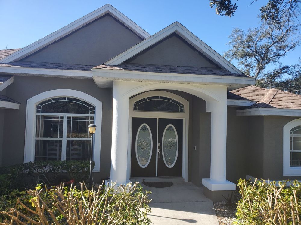 Gray house with white trim and columns, arched windows, and double doors.
