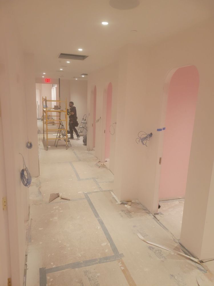 Construction in a pink-walled hallway with arched doorways. A worker stands near scaffolding.
