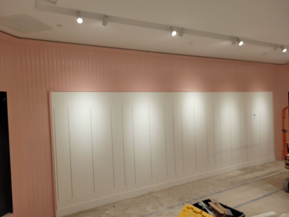 A retail space wall with white paneling lit by spotlights, against a pink upper wall.