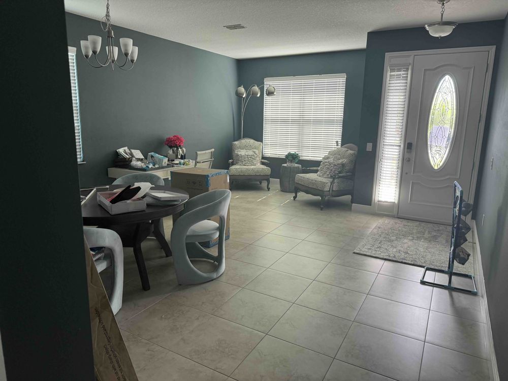 Living room with teal walls, beige tile, and white door. Furniture includes chairs, a coffee table, and a dining table.