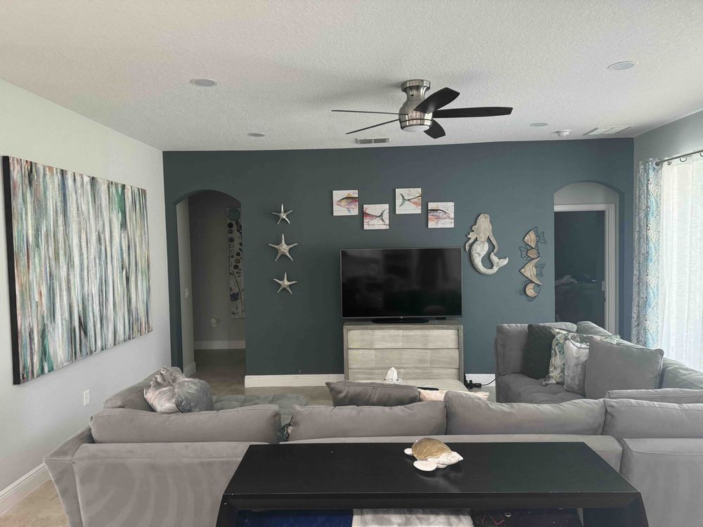 Living room with gray sectional, teal accent wall, TV, and decorative seashells.