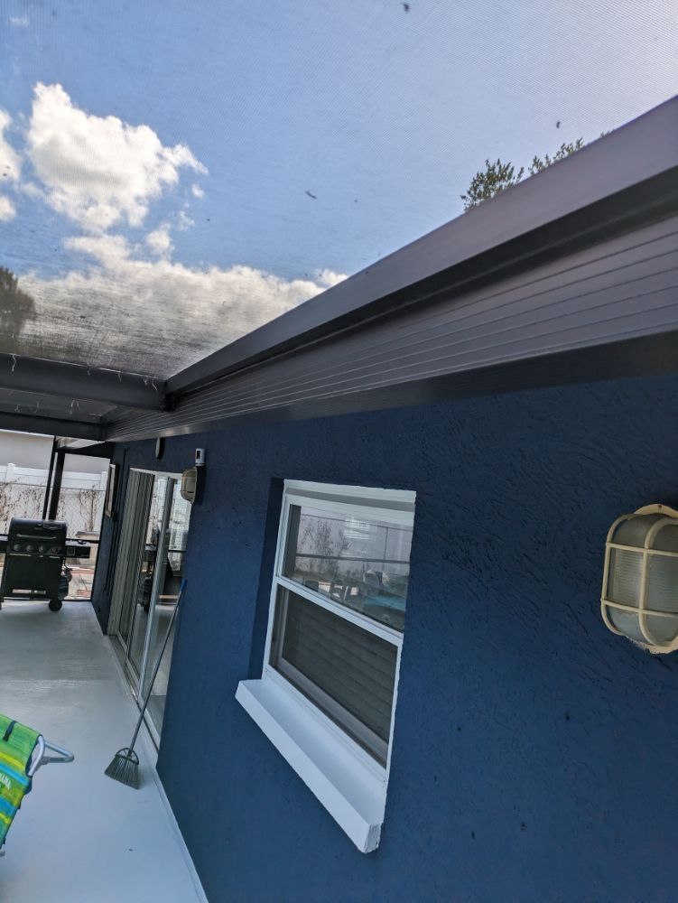Blue house exterior with dark trim, white window, and cloudy sky.