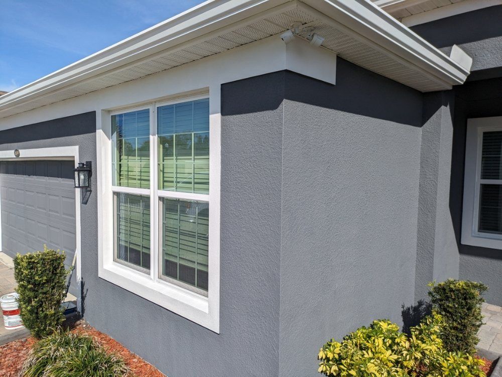 Gray house exterior with white trim, a window, and greenery.