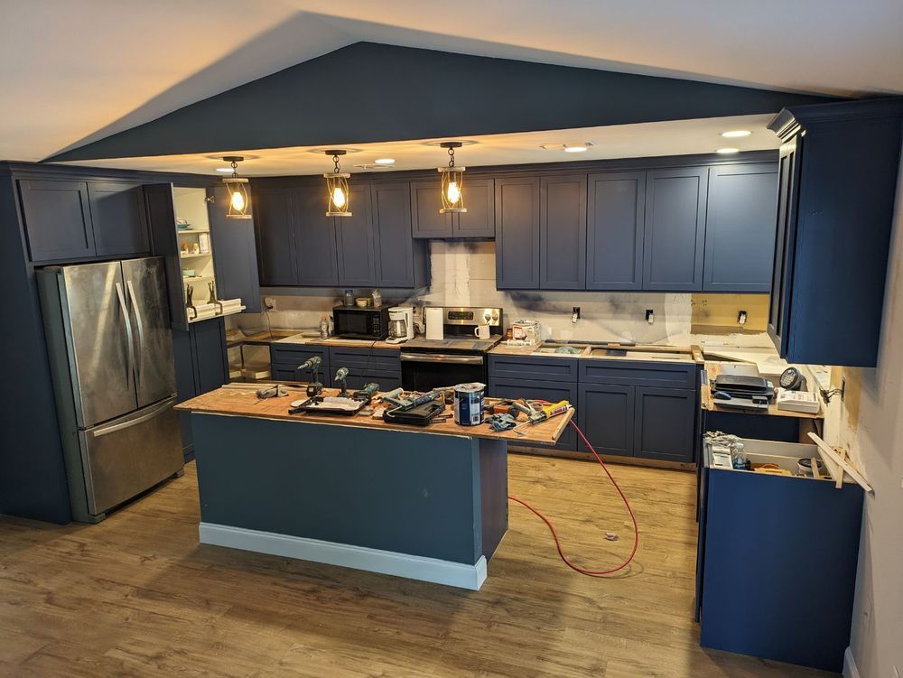 Navy blue kitchen cabinets with island and stainless steel fridge, under construction.