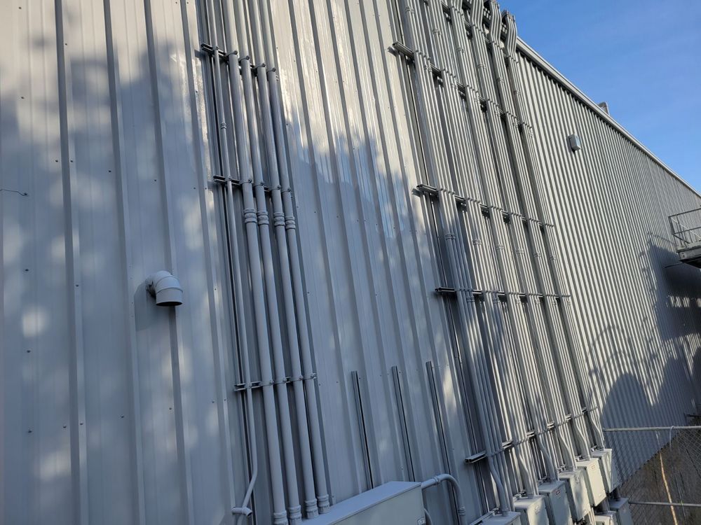 Exterior of industrial building with corrugated metal siding; conduit lines run up the side.