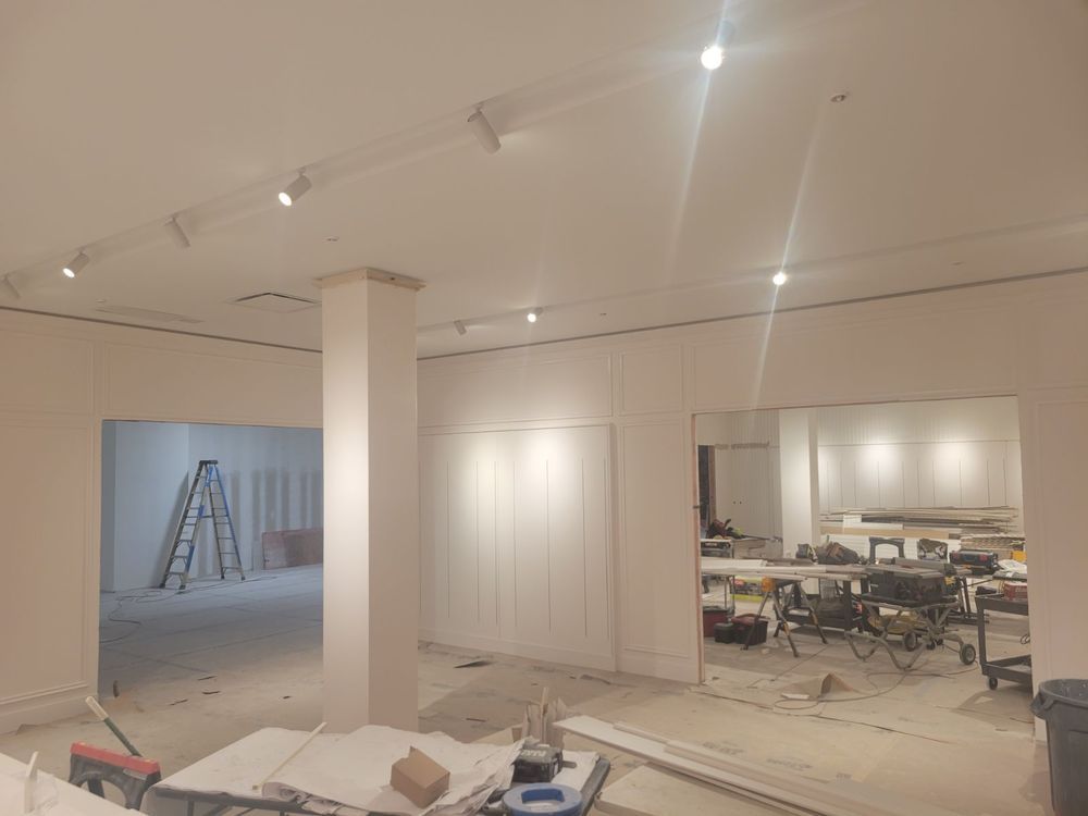 Interior of a building under construction, with white walls, lighting fixtures, and open doorways.