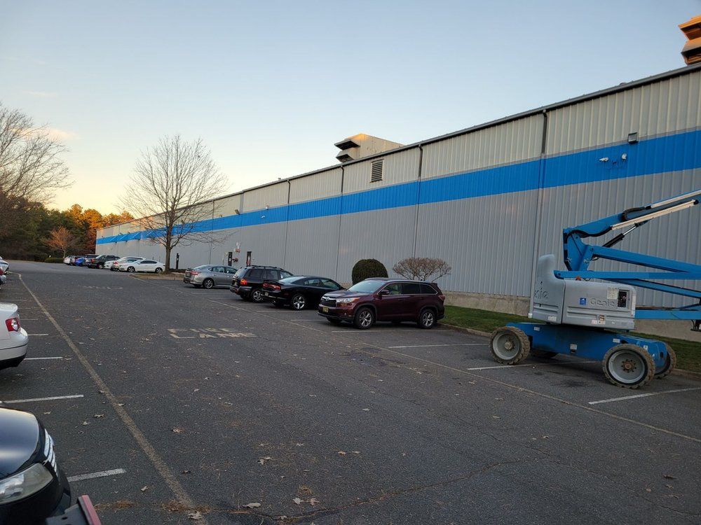 Cars parked in front of a large industrial building with a blue stripe. A lift platform is on the right.