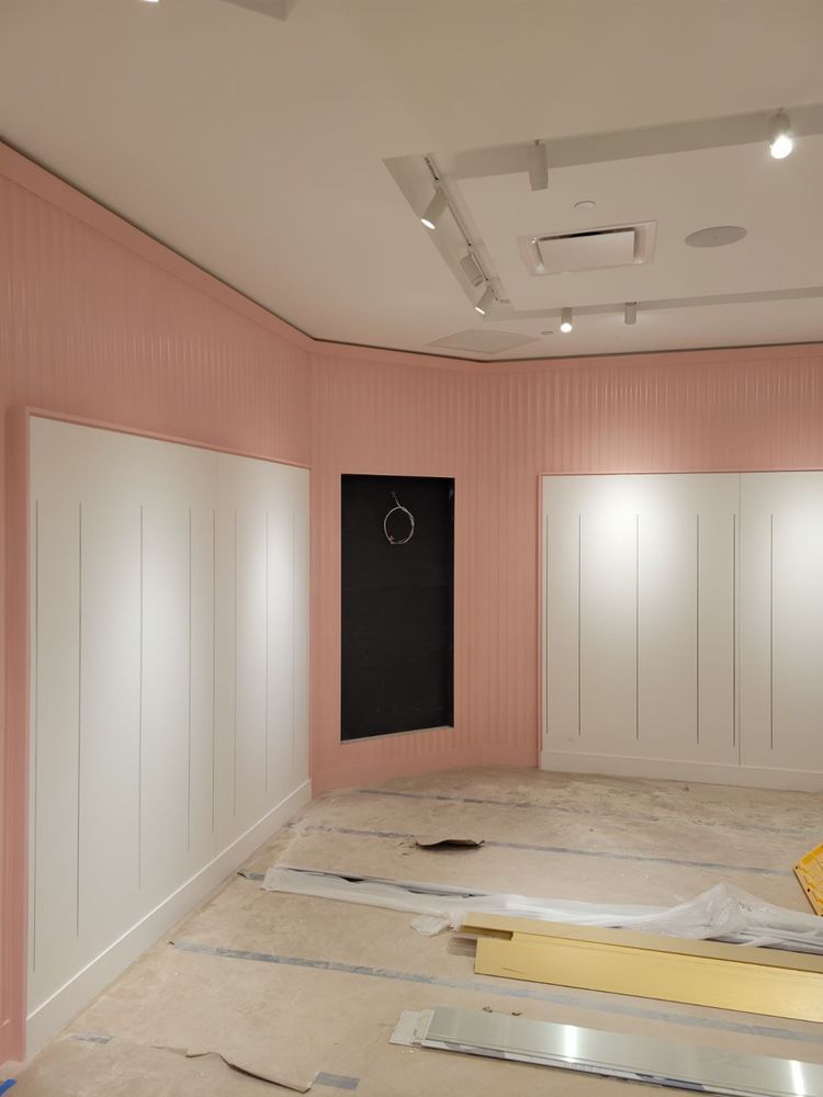 Empty room under construction, pink and white walls, black door, track lighting, unfinished floor.
