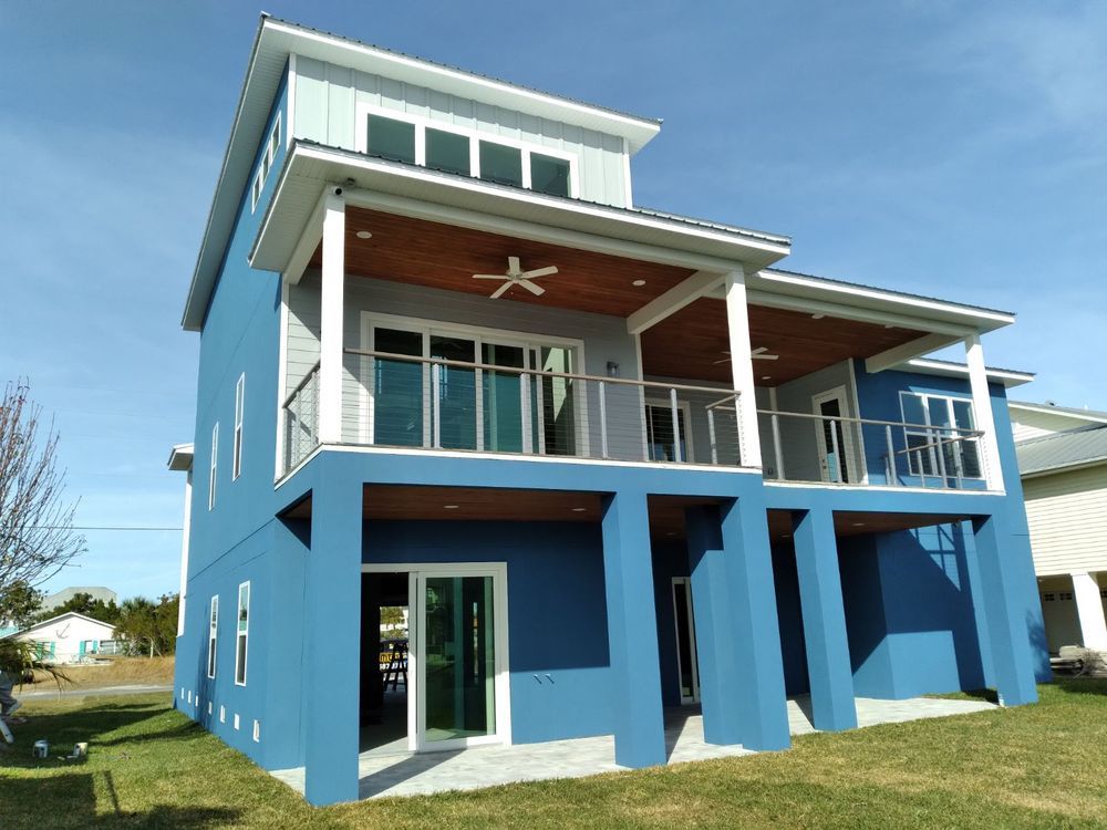 Blue house with two-story porch, clear glass railings, light wood ceiling, and blue sky.