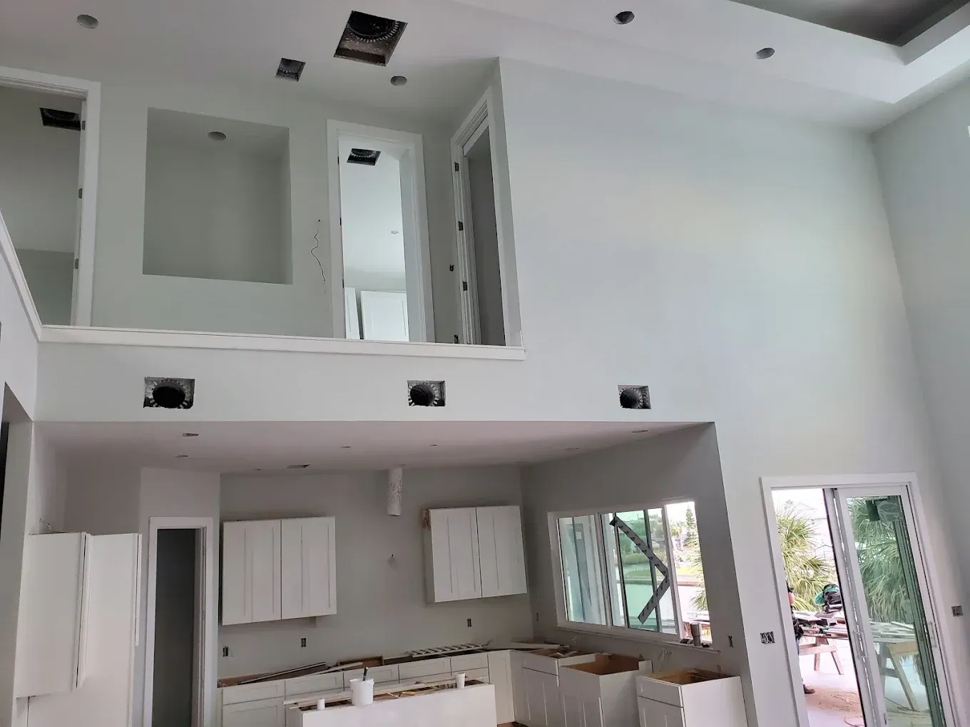 Interior of a home under construction, kitchen with cabinets, a balcony overlooking the kitchen area, white walls.