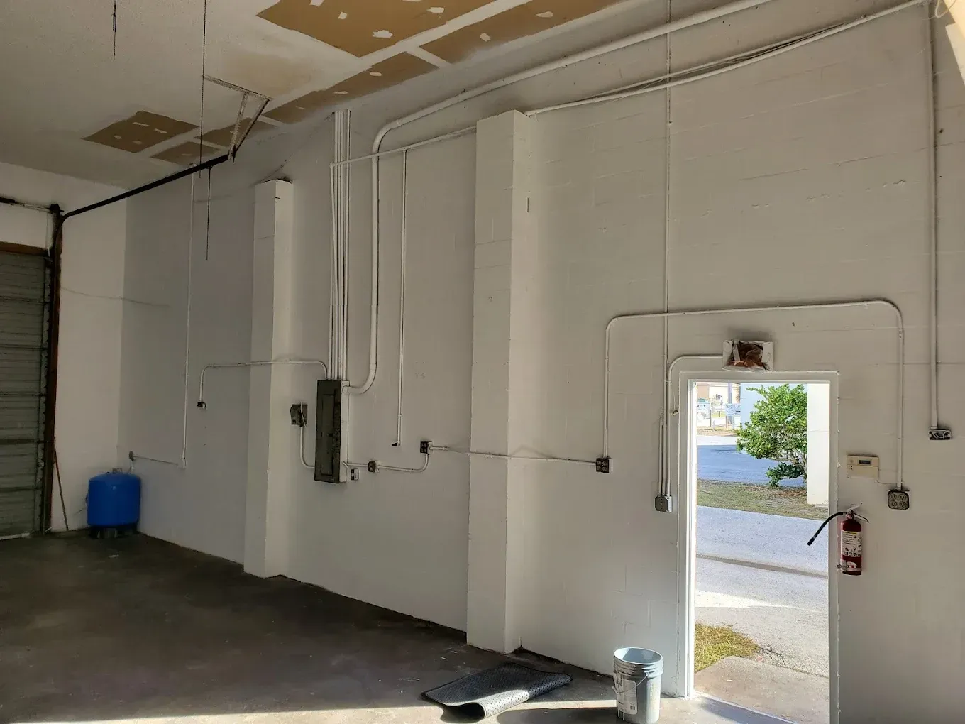 Interior view of a commercial space with conduit wiring and a door. Blue water tank visible.