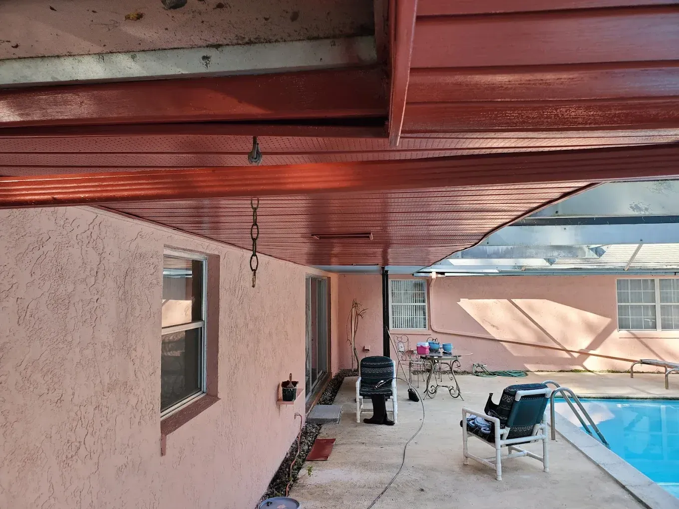 Exterior view of a patio with a red-painted ceiling, overlooking a pool and pink stucco wall.