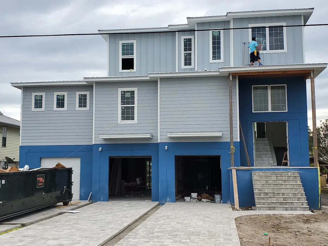 Multi-story house under construction; blue and gray siding, person on roof.
