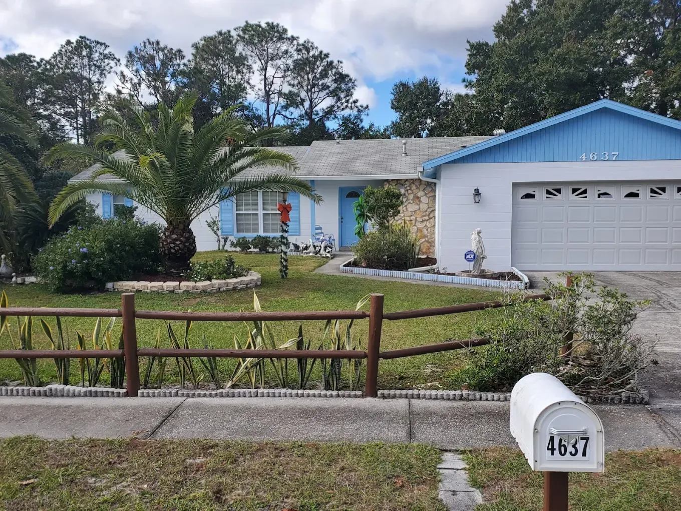 White house with blue trim, a brown fence, and a mailbox.