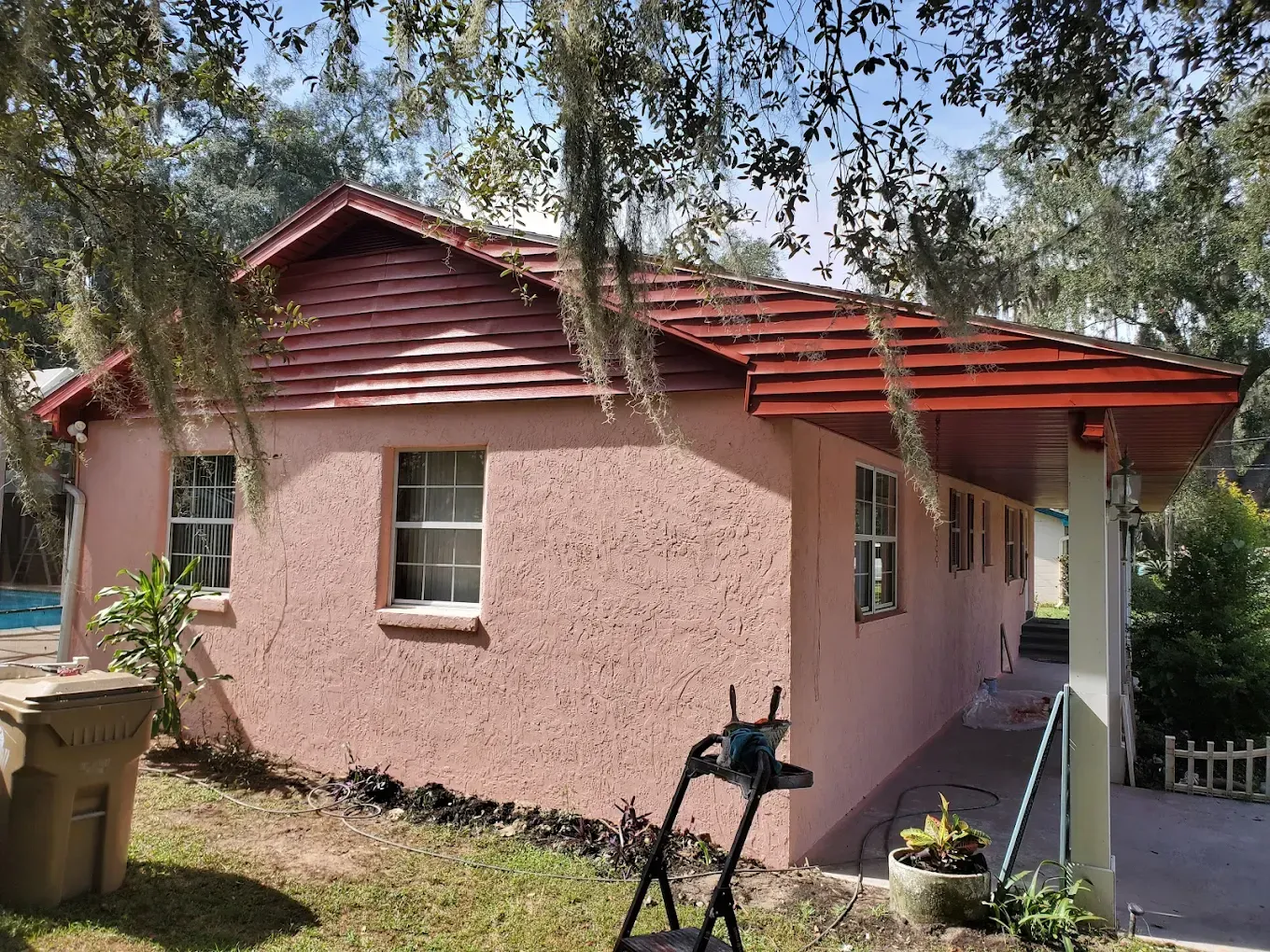 Pink stucco house with red roof, windows, and porch, in a sunny outdoor setting.