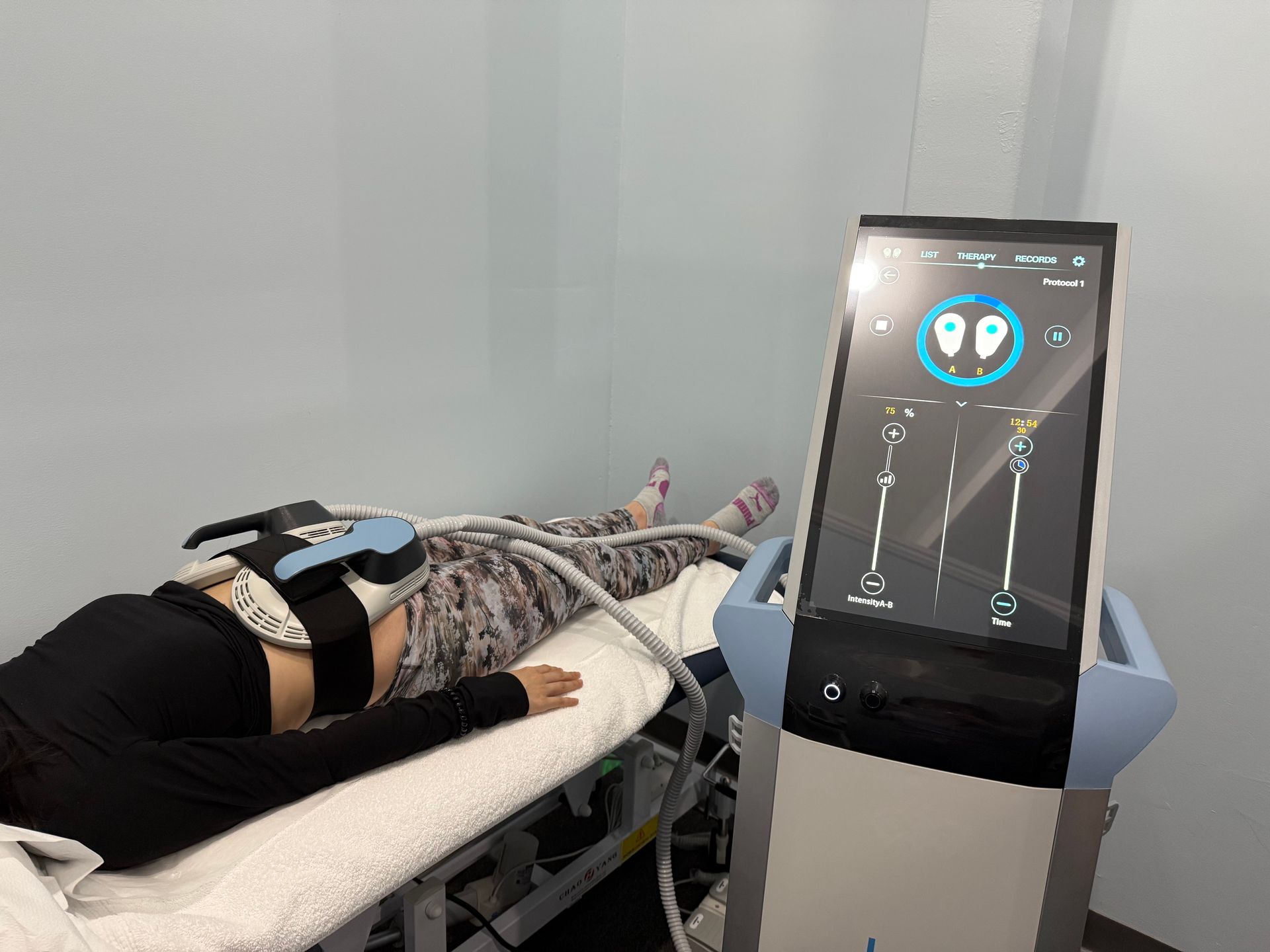 A woman is laying on a bed in front of a machine.