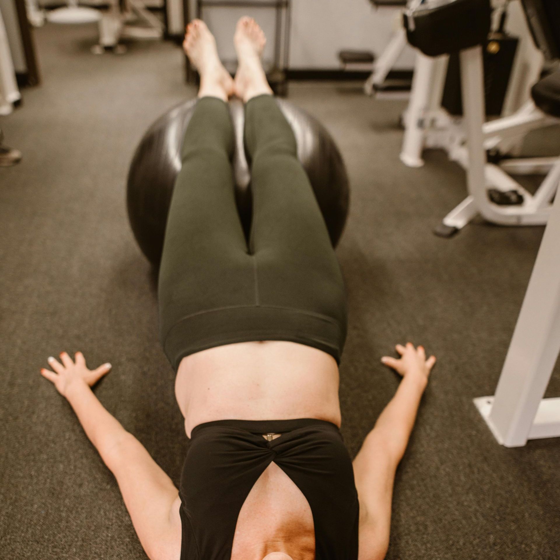 A woman is laying on her back on a pilates ball in a gym.