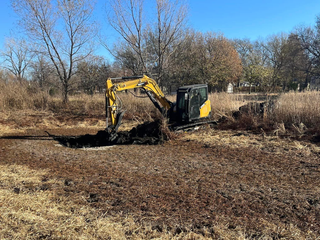 A Yellow Excavator Is Digging a Hole in A Field | Independence, KS | K & M Pasture Clearing and Skid Loader Services