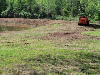A Tractor Is Driving Through a Grassy Field Next to A Pond | Independence, KS | K & M Pasture Clearing and Skid Loader Services