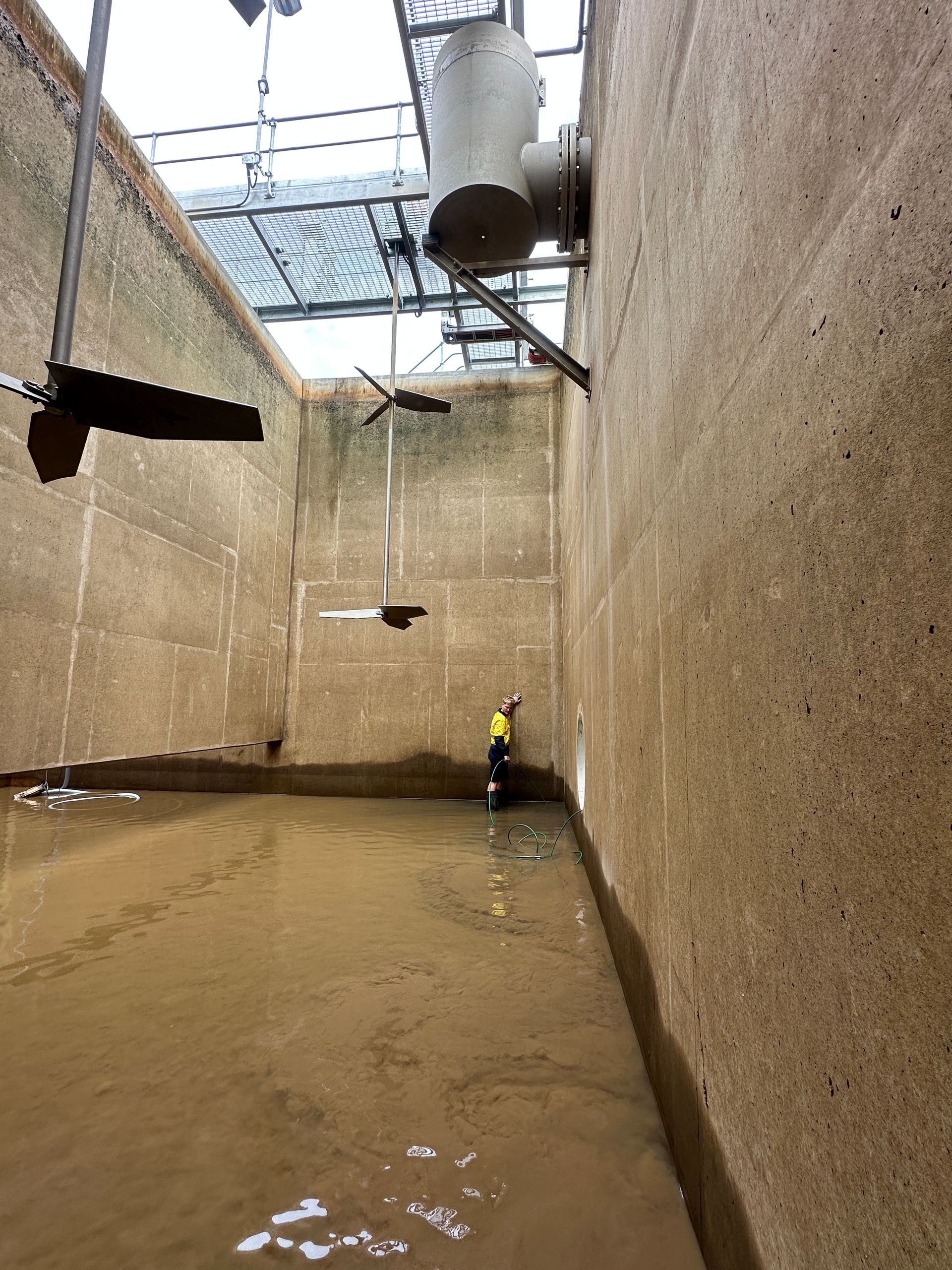 Concrete Tank With Brown Water, Mixers, and a Worker in High-vis Vest — Northern Plumbing In Kirwan, QLD