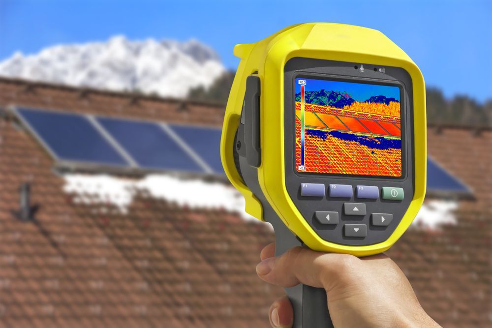 A Person Is Holding A Thermal Camera In Front Of A Roof With Solar Panels — Northern Plumbing In Mount Louisa, QLD
