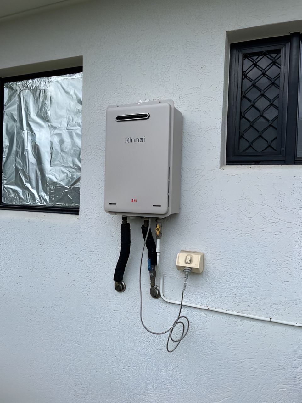 A Water Heater Is Hanging On The Side Of A Building Next To A Window — Northern Plumbing In Mount Louisa, QLD