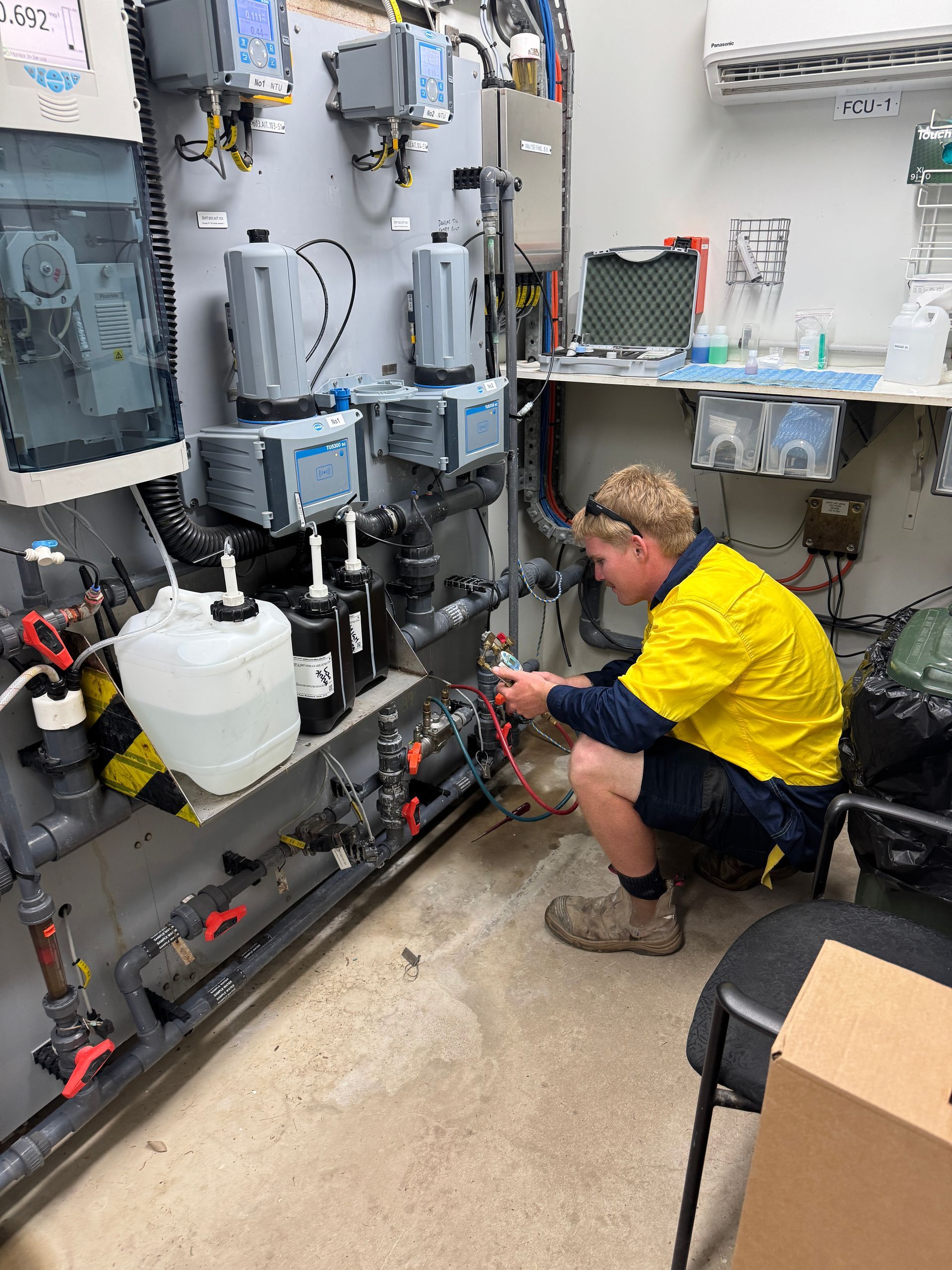 A Person in a Yellow Shirt Crouches to Work on Water Treatment Equipment — Northern Plumbing In Kirwan, QLD
