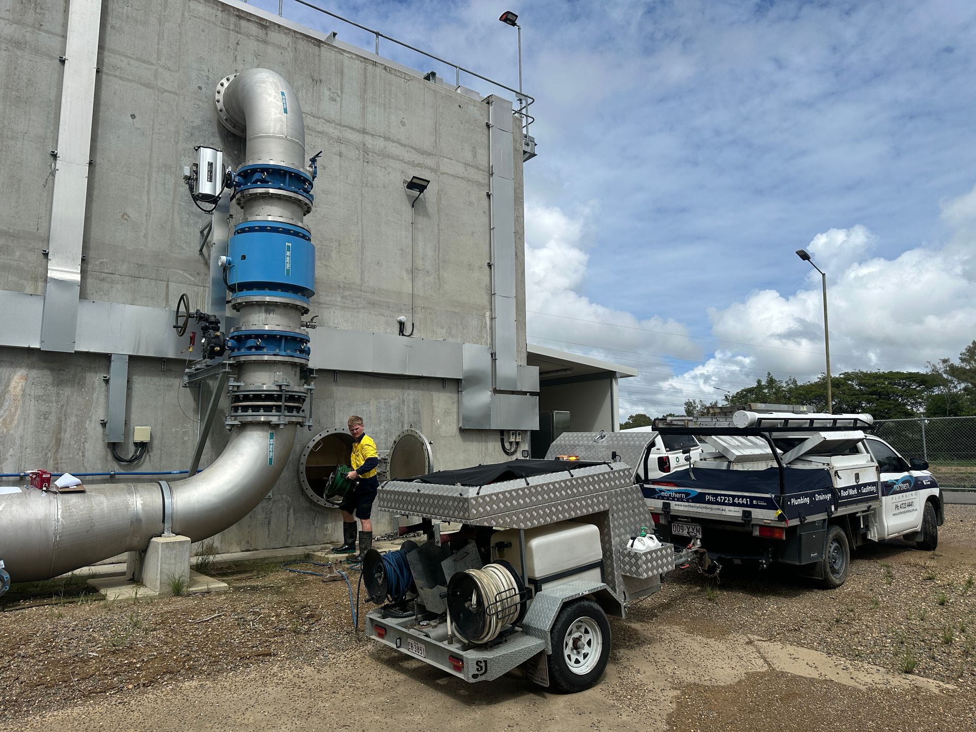 Man Working on Large Water Pipes Attached to a Concrete Building — Northern Plumbing In Mount Louisa, QLD