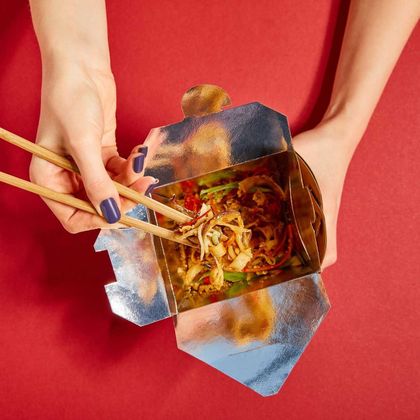 Woman holding wooden chopsticks near tasty noodles on red