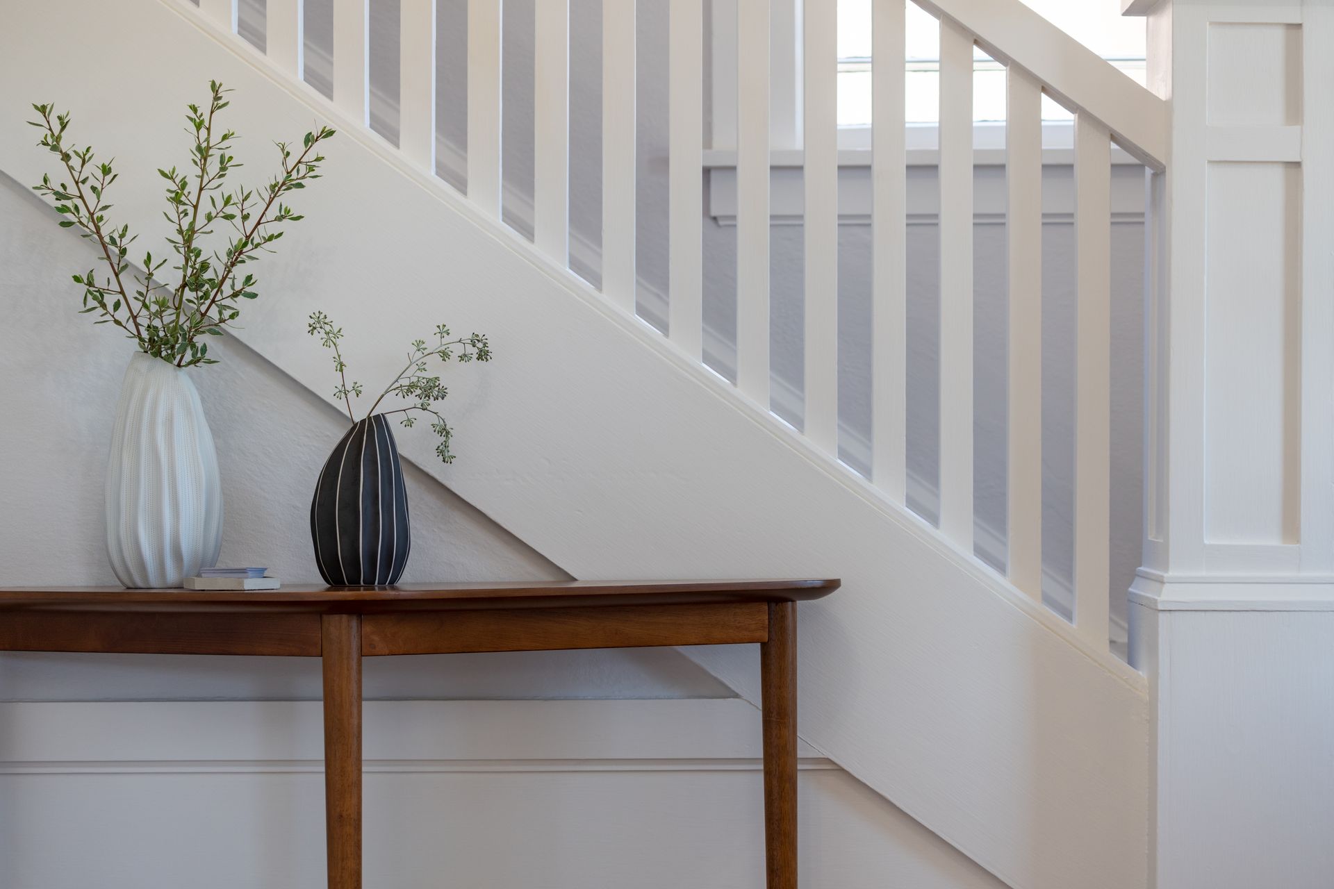 A vase of flowers is sitting on a wooden table next to a staircase.