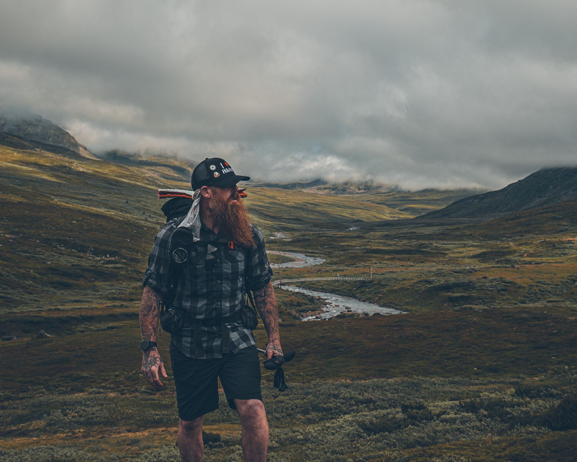 A man with a beard and a backpack is standing in a field.