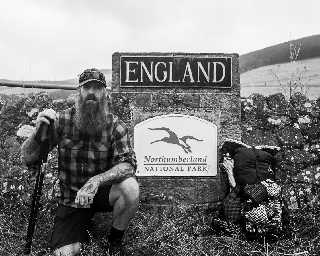 A man with a beard is kneeling in front of a sign that says england.