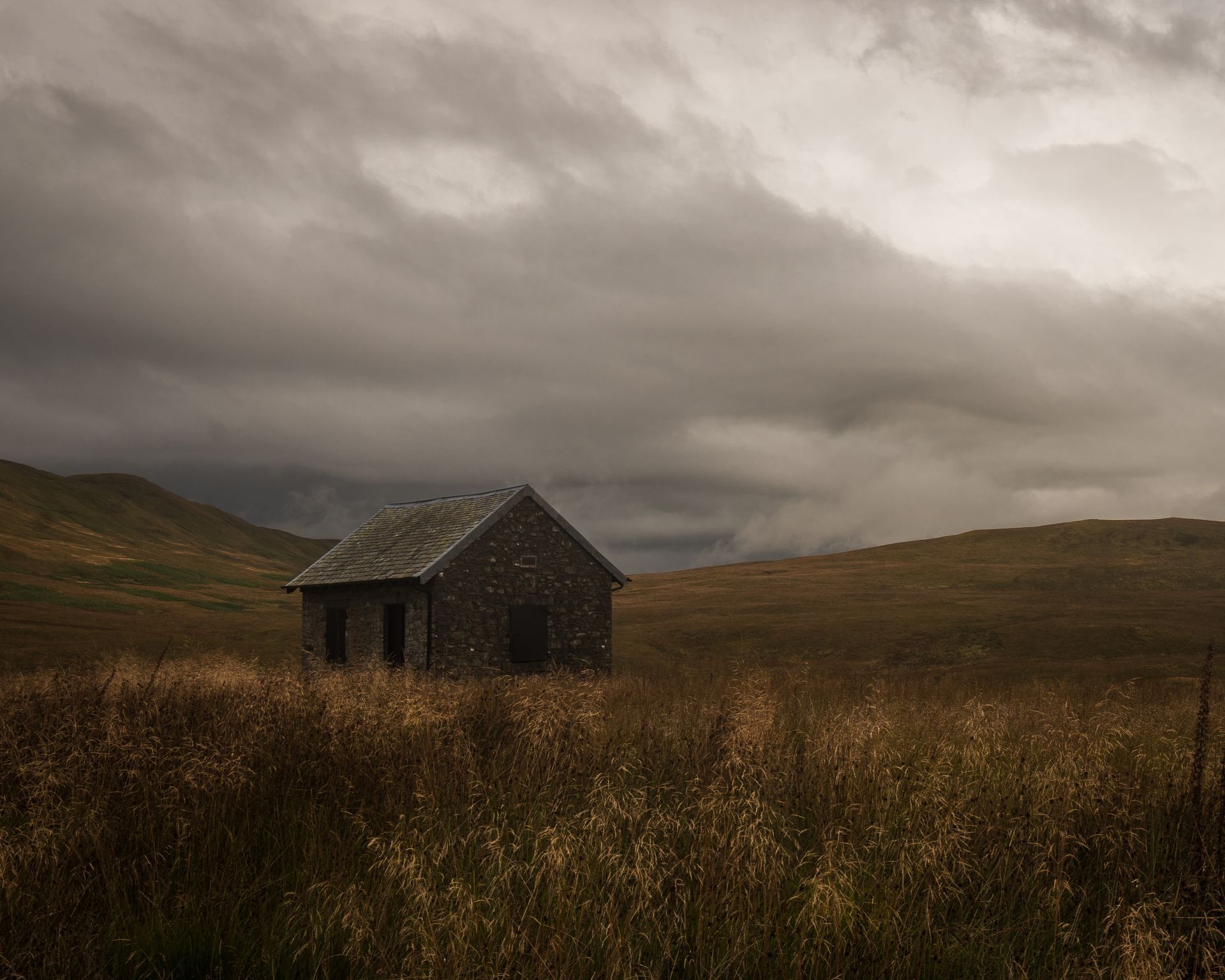 A small house is sitting in the middle of a field on a cloudy day.