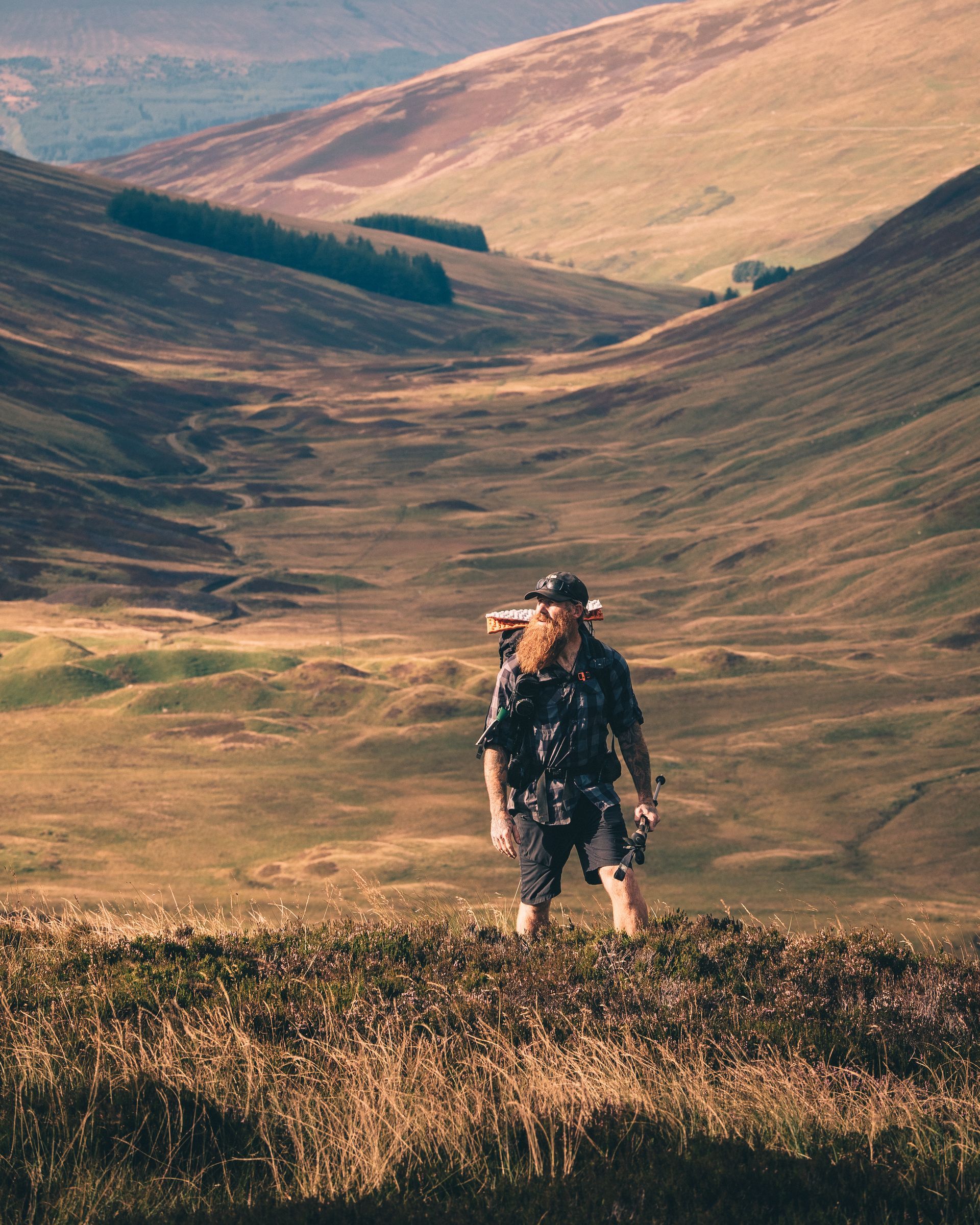 A man is standing on top of a hill with a dog on his back.