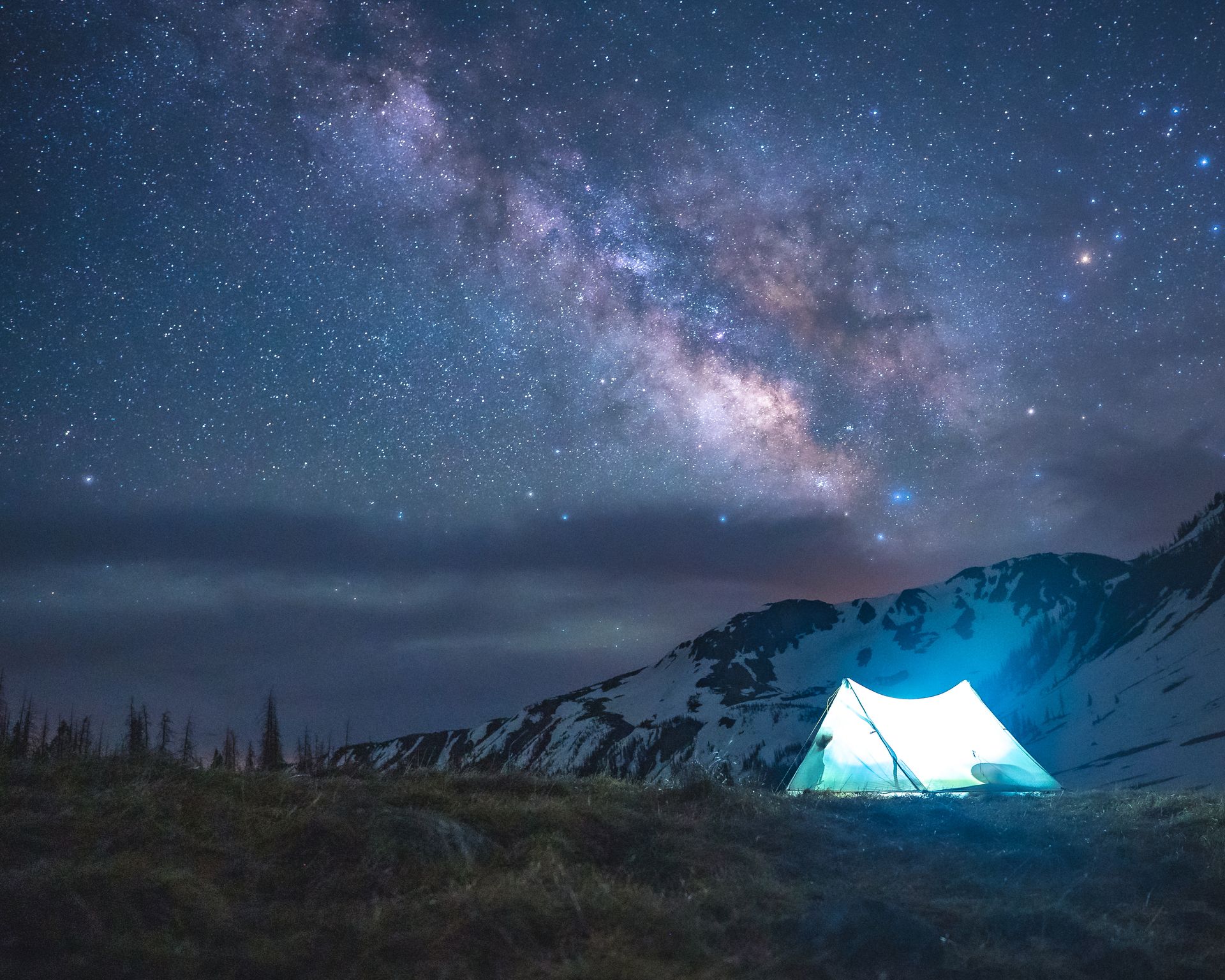 A tent is lit up under a starry night sky