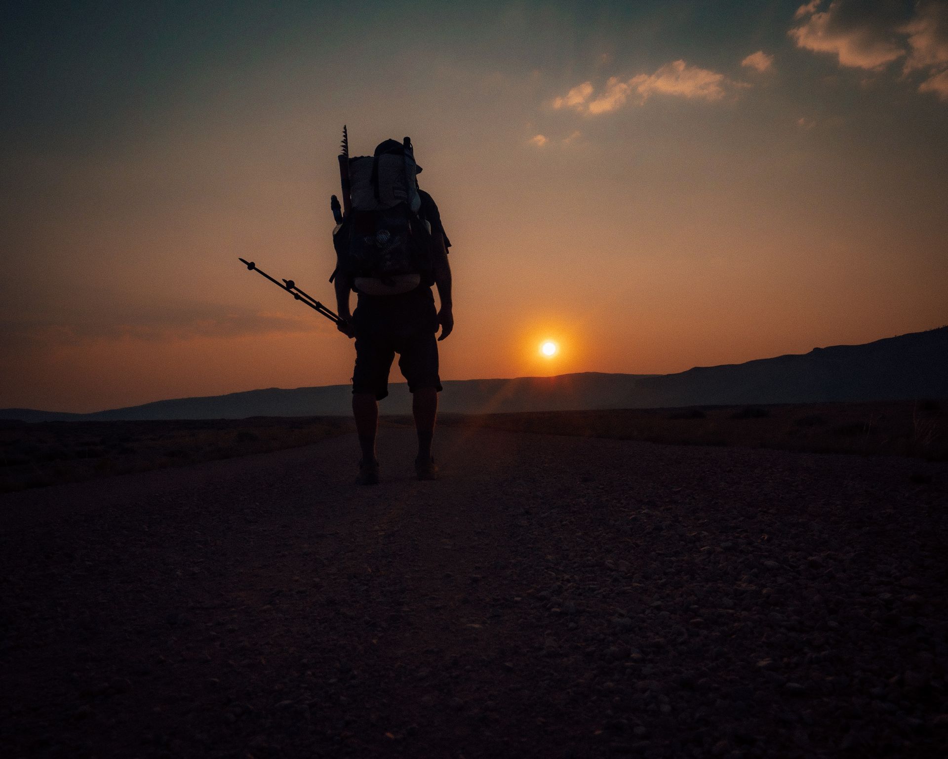 A man with a backpack is standing in the desert at sunset.